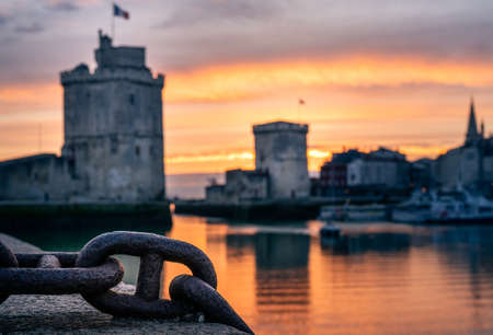 The old harbor of La Rochelle at sunset with its famous old towers. beautiful orange sky. Chain on the foregroundの写真素材