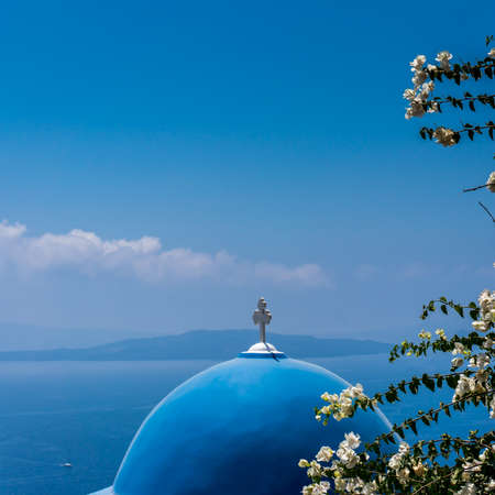 Detail of a blue church roof in Santorini island, Greece .. Bougainvillea white flowers on the foreground. Blue sea and sky in the background. Square formatの写真素材