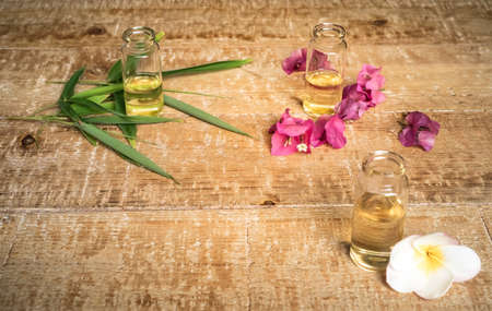 Essential oil in small glass bottles with bamboo leaves, bougainvillea and frangipani flowers on wooden background. Selective focus. top view and copy space for text. Natural cosmetics.の写真素材