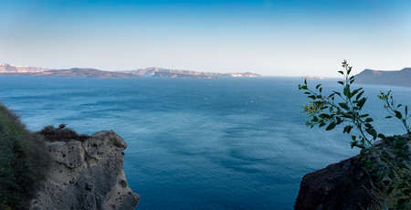 Beautiful panoramic view from Oia to caldera and volcano on a sunny day. Picturesque natural background with copy space for text. Santorini island, Cyclades, Greece, Europe.の写真素材