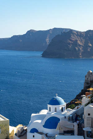 View of Santorini, with typical blue dome church, caldera, sea and flags. Portrait formatの写真素材