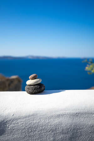 Close-up shot of pebbles stacked on each other in a balance with santorini caldera in the backgroundの写真素材