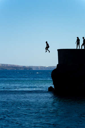 Group of friends jumping into mediterranean sea from rock cliffの写真素材