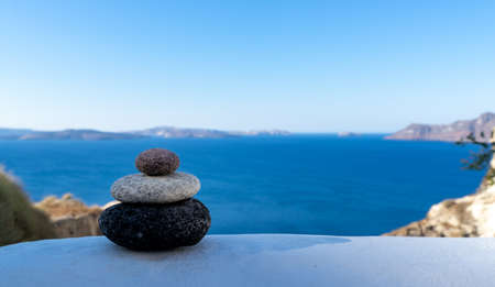 Close-up shot of pebbles stacked on each other in a balance with santorini caldera in the backgroundの写真素材