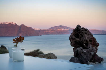 Candle and plant decoration on a white table. Oia, Santorini island, Greece. Beautiful sunset colors on the caldera.の写真素材