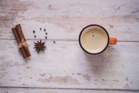 Top view of a vintage orange coffee cup with cinnamon and star anise on a white wooden background....