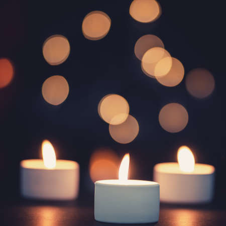 Three burning candles in front of a beautiful colorful circle shiny bokeh backgroundの写真素材