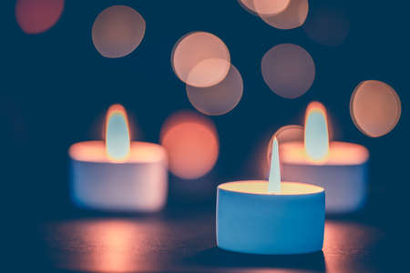Three burning candles in front of a beautiful colorful circle shiny bokeh backgroundの写真素材