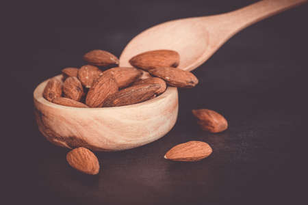 Almonds in a wooden bowl with a wooden spoon on a black table. Close-up and minimalist shot with vintage tonesの写真素材