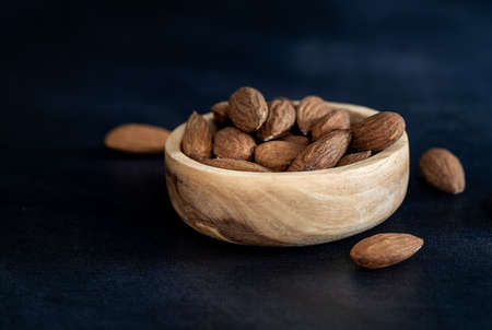 Almonds in a wooden bowl with a wooden spoon on a black table. Close-up and minimalist shot. Eco friendly conceptの写真素材