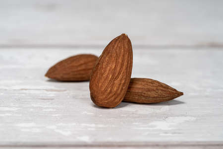 Close-up of three isolated almonds standing up on a white wooden table in a white background. Close-up and minimalist shot with copy space for textの写真素材