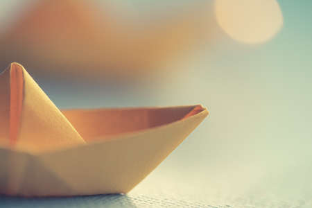 Origami yellow sailing boat on a sea made with blue paper. Paper art style background with ship, ocean and bokeh lightsの写真素材