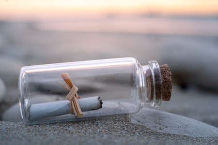 close-up view of a small glass bottle containing a paper message. The bottle is lying on the beach at sunrise.の写真素材