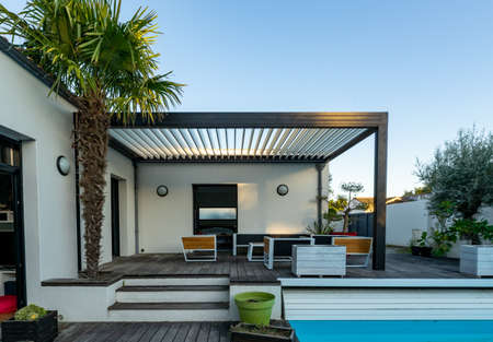Trendy outdoor patio pergola shade structure, awning and patio roof, garden lounge, chairs, metal grill surrounded by landscapingの写真素材