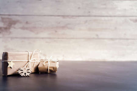 Christmas and zero waste, eco friendly packaging. wrapped gifts in craft paper with wooden snowflakes and star on a wooden background. ecological Christmas holiday concept, eco decor with woodの写真素材