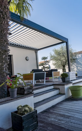 Trendy outdoor patio pergola shade structure, awning and patio roof, garden lounge, chairs, metal grill surrounded by landscapingの写真素材