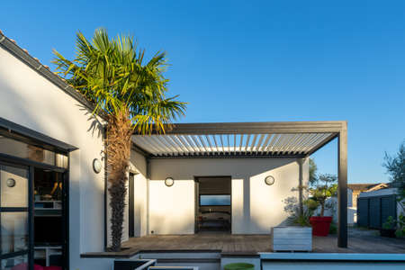 Trendy outdoor patio pergola shade structure, awning and patio roof, garden lounge, chairs, metal grill surrounded by landscapingの写真素材