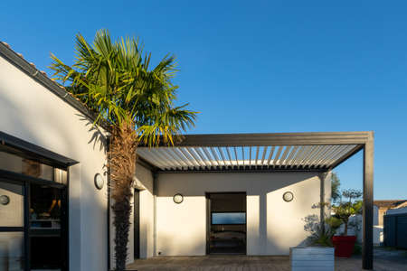Trendy outdoor patio pergola shade structure, awning and patio roof, garden lounge, chairs, metal grill surrounded by landscapingの写真素材