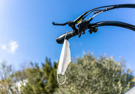 Surgical face mask hanging on a bicycle handlebar ready to be used in the city, protection against covid-19 infection during coronavirus pandemic, copy space, selected focusの写真素材