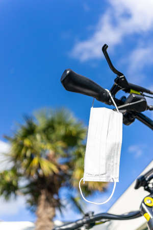 Surgical face mask hanging on a bicycle handlebar ready to be used in the city, protection against covid-19 infection during coronavirus pandemic, copy space, selected focusの写真素材