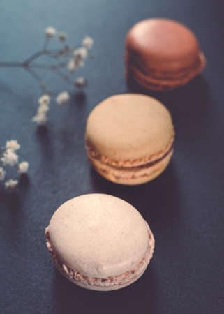 A dark, moody image of chocolate, caramel, and vanilla macaroons arranged on a slate tile, atop a...