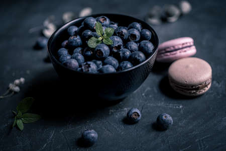 close-up of fresh blueberries in a black bowl with macaroons around on a black slate. the macaroon a small French almond cake. close-up viewの写真素材