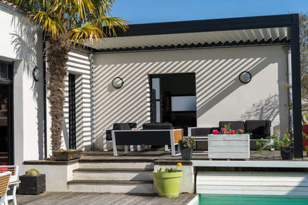 Trendy outdoor patio pergola shade structure, awning and patio roof, garden lounge, chairs, metal grill surrounded by landscapingの写真素材