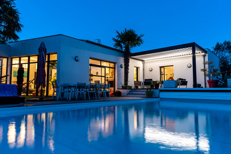 Trendy outdoor patio pergola shade structure, awning and patio roof, garden lounge, chairs, metal grill surrounded by landscaping. night shotの写真素材