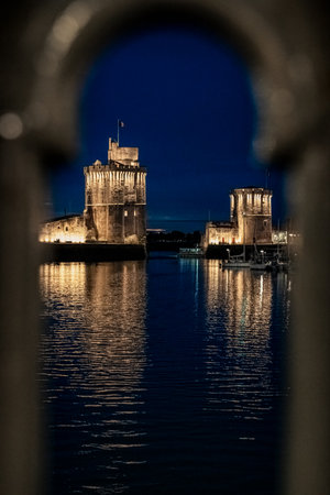 view through balustrade of the old harbor of La Rochelle at night with its famous old towers.の写真素材