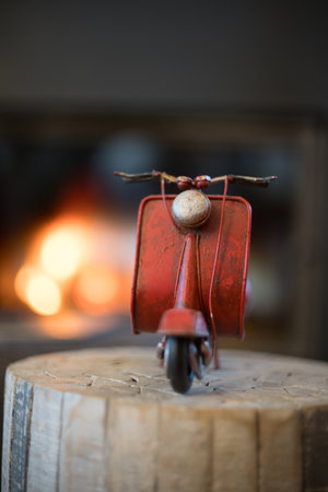Vintage red scooter on a wooden stand with an orange light in the background, like an open fire.の写真素材