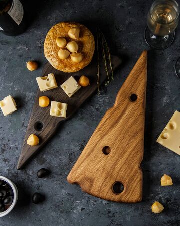 Wooden cheese boards in the form of a piece of cheese with holes with cheese toppedの写真素材
