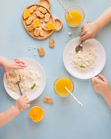 Children have breakfast with cottage cheese with orange juice and cookies on a blue table, top viewの写真素材