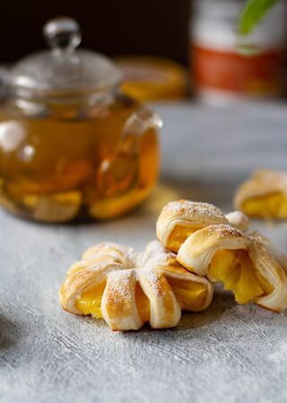 Puffs with pineapple on a gray table, in the background a glass teapot with tea, yellow.の写真素材