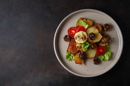 Fried vegetables: potatoes, zucchini, tomatoes and grilled mushrooms with fresh herbs, on a dark...