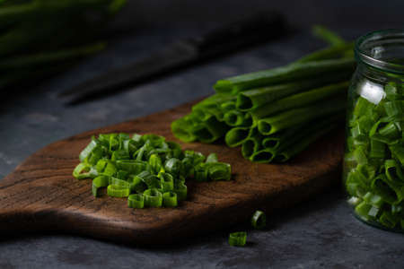 Sliced â€‹â€‹onion greens on a wooden board on a dark table