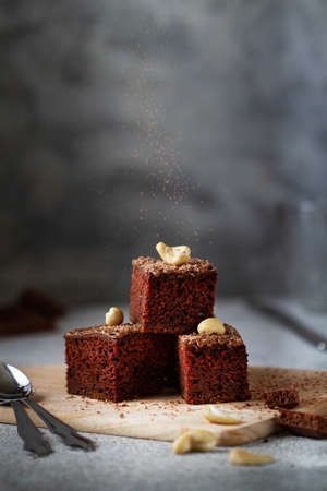 diced chocolate brownie lies on a board on a gray table. Cocoa powder is poured. Close-up