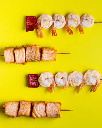 Shrimp and salmon kebabs on skewers on a bright yellow background, top view, pattern, seafood