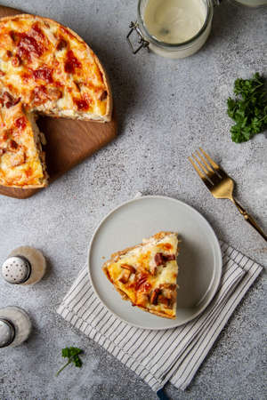 Quiche lauren with mushrooms, chicken and cheese with a cut out piece on a gray table, top view, next to greens and kitchenware, light photoの写真素材