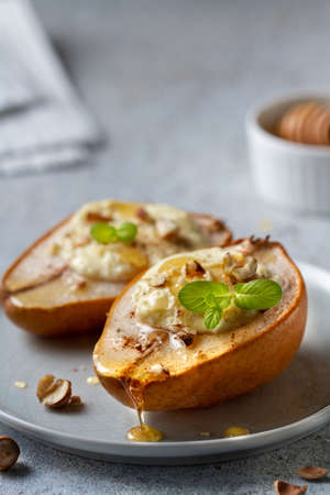 Two baked pears stuffed with cottage cheese and nuts lie on a plate, poured honey on top from a honey spoonの写真素材