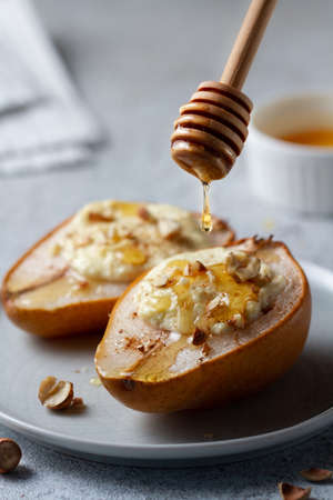 Two baked pears stuffed with cottage cheese and nuts lie on a plate, poured honey on top from a honey spoonの写真素材