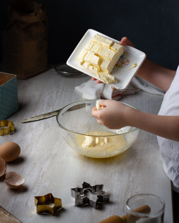 The child prepares dough for cookies, puts pieces of butter in a glass transparent cup with dough. Gray table.の写真素材