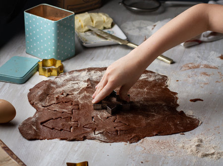 Children's hands cut out cookies in the form of Christmas trees and snowflakes from chocolate dough on a gray tableの写真素材