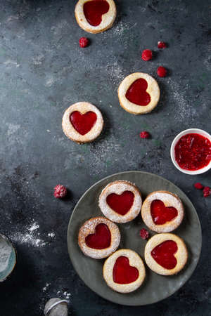 Linzer cookies with raspberry jam, red hearts on a blue table. A mess, berries are lying, powder is...