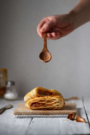 Pieces of puff pastry with filling lie on a wooden board. Hand with a wooden spoon pours caraway...