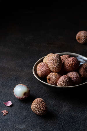 Pink lychees in a ceramic bowl on a dark brown background. Free place.