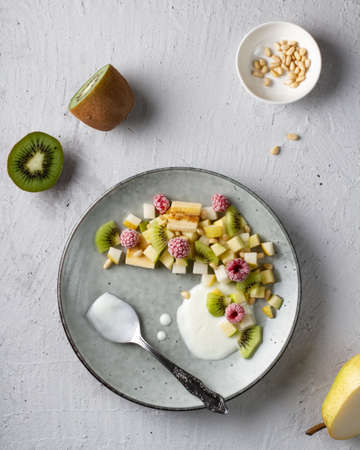 Fruit salad with raspberries and kiwi seasoned with white yogurt on a gray plate, on the table, top view.の写真素材