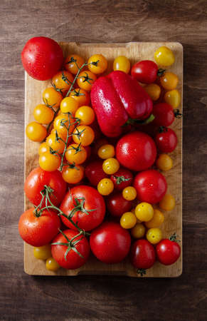 Red and yellow tomatoes, large and cherry on a branch, peppers on a wooden board, a lot, top view.の写真素材