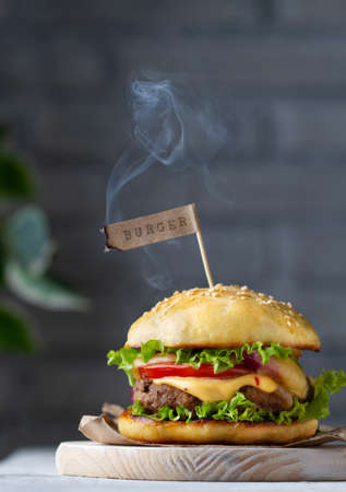 Classic burger with paper flag with lettering and smoke on chalkboard, close-up