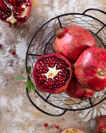 Ripe pomegranates in a metal basket, with leaves, on a concrete table, top view