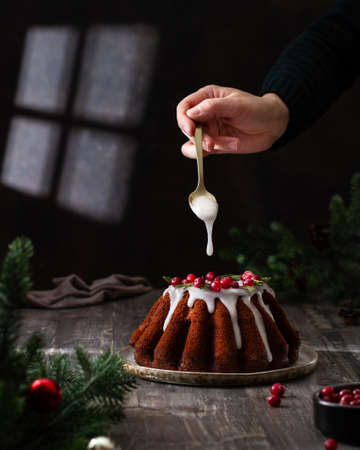 Chocolate cupcake with cranberries and rosemary on the table, hand pours icing, atmosphere, christmasの写真素材